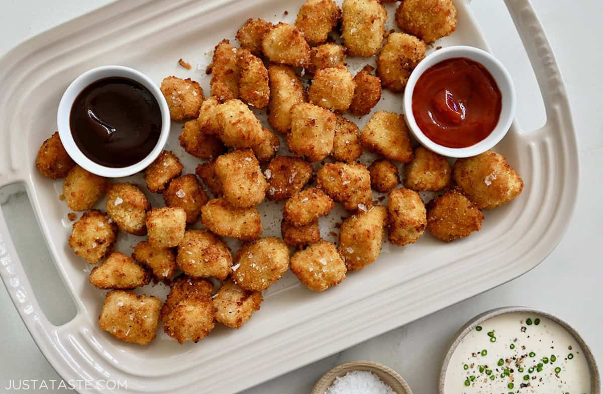 A white platter containing air fryer chicken nuggets with small bowls of dipping sauces.