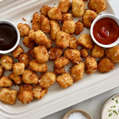 A white platter containing air fryer chicken nuggets with small bowls of dipping sauces