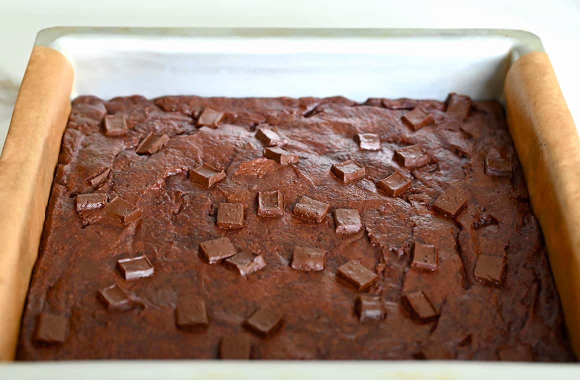 Freshly baked brownies topped with chocolate chunks in a parchment paper-lined baking dish