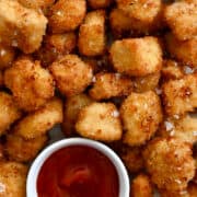 A close-up view of air fryer chicken nuggets surrounding two small bowls containing ketchup and Ranch dressing.