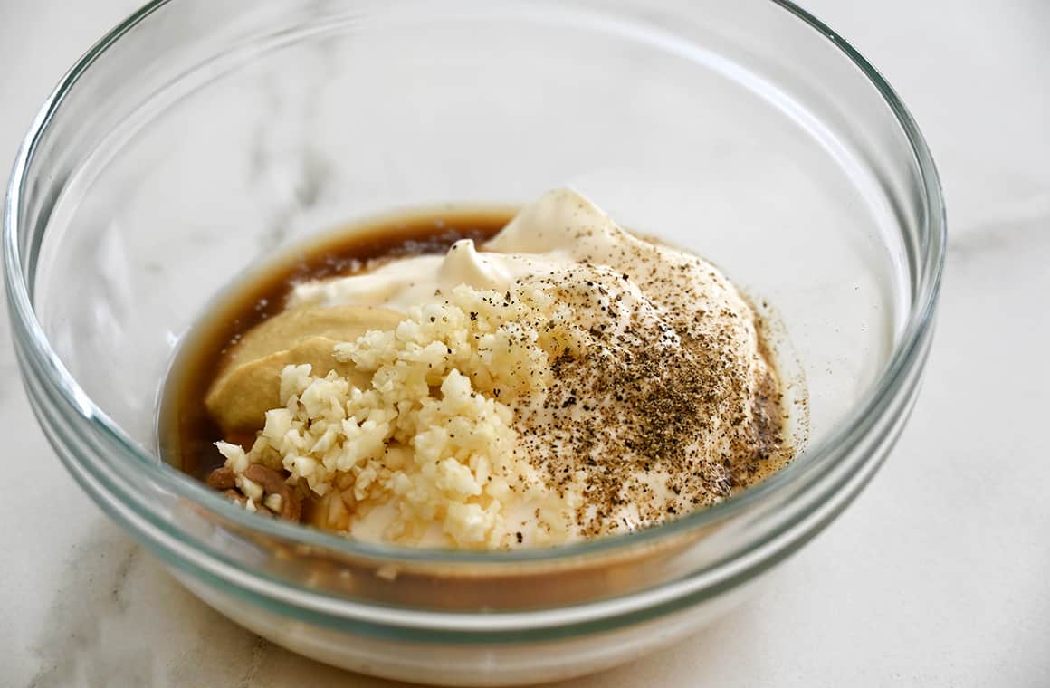 A glass bowl containing ingredients for homemade Caesar salad dressing