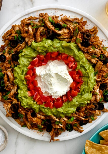 A white platter with taco dip surrounded by bowls of chips and seasonings