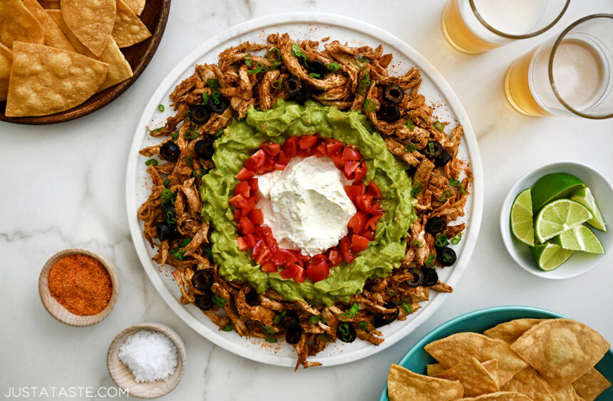 A white platter with taco dip surrounded by bowls of chips and seasonings