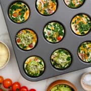 A top-down view of a muffin tin containing egg white muffins with spinach, yellow peppers and tomatoes.