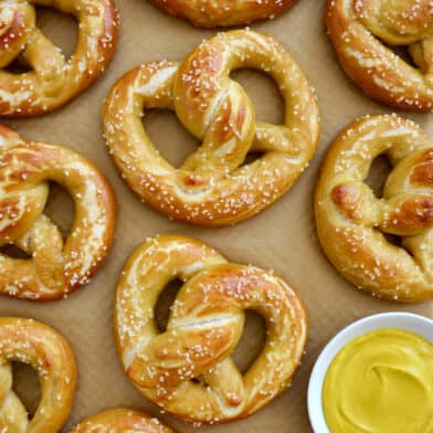 Homemade soft pretzels on brown parchment paper next to a small bowl containing yellow mustard.