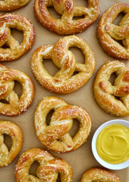 Homemade soft pretzels on brown parchment paper next to a small bowl containing yellow mustard.