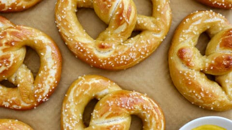 Homemade soft pretzels on brown parchment paper next to a small bowl containing yellow mustard.