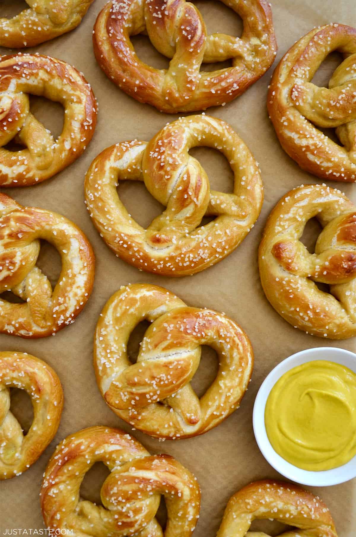 Homemade soft pretzels on brown parchment paper next to a small bowl containing yellow mustard.