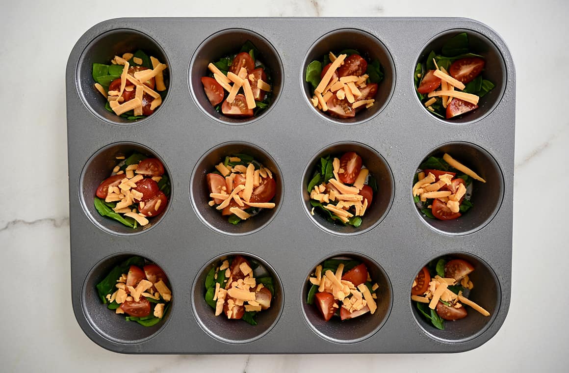 A muffin pan containing diced veggies and shredded cheese