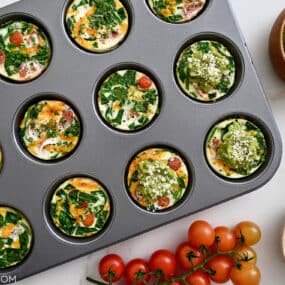 A top down view of a muffin pan containing egg muffins surrounded by cherry tomatoes and avocado