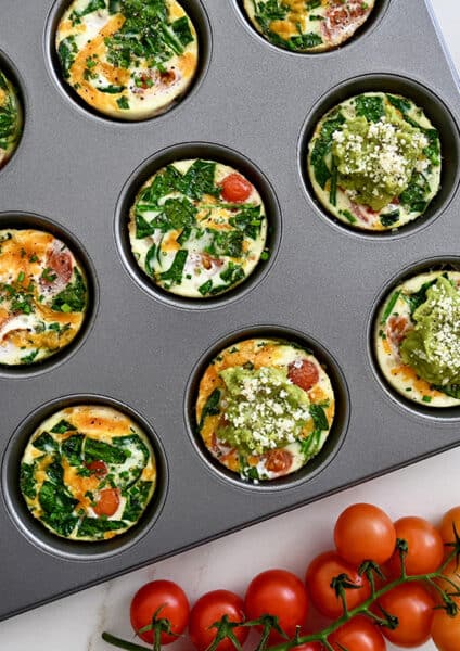 A top down view of a muffin pan containing egg muffins surrounded by cherry tomatoes and avocado