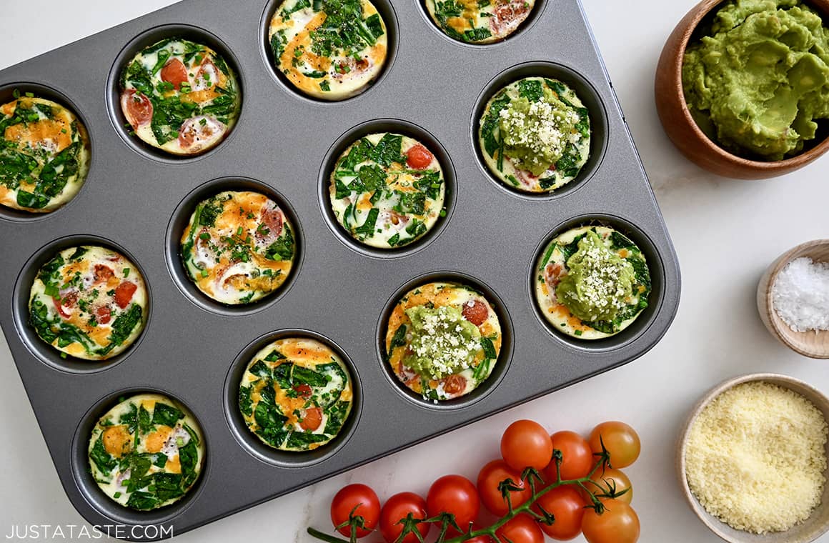 A top down view of a muffin pan containing egg muffins surrounded by cherry tomatoes and avocado