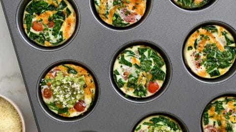 A top-down view of a muffin pan with egg white muffins, tomatoes and avocado