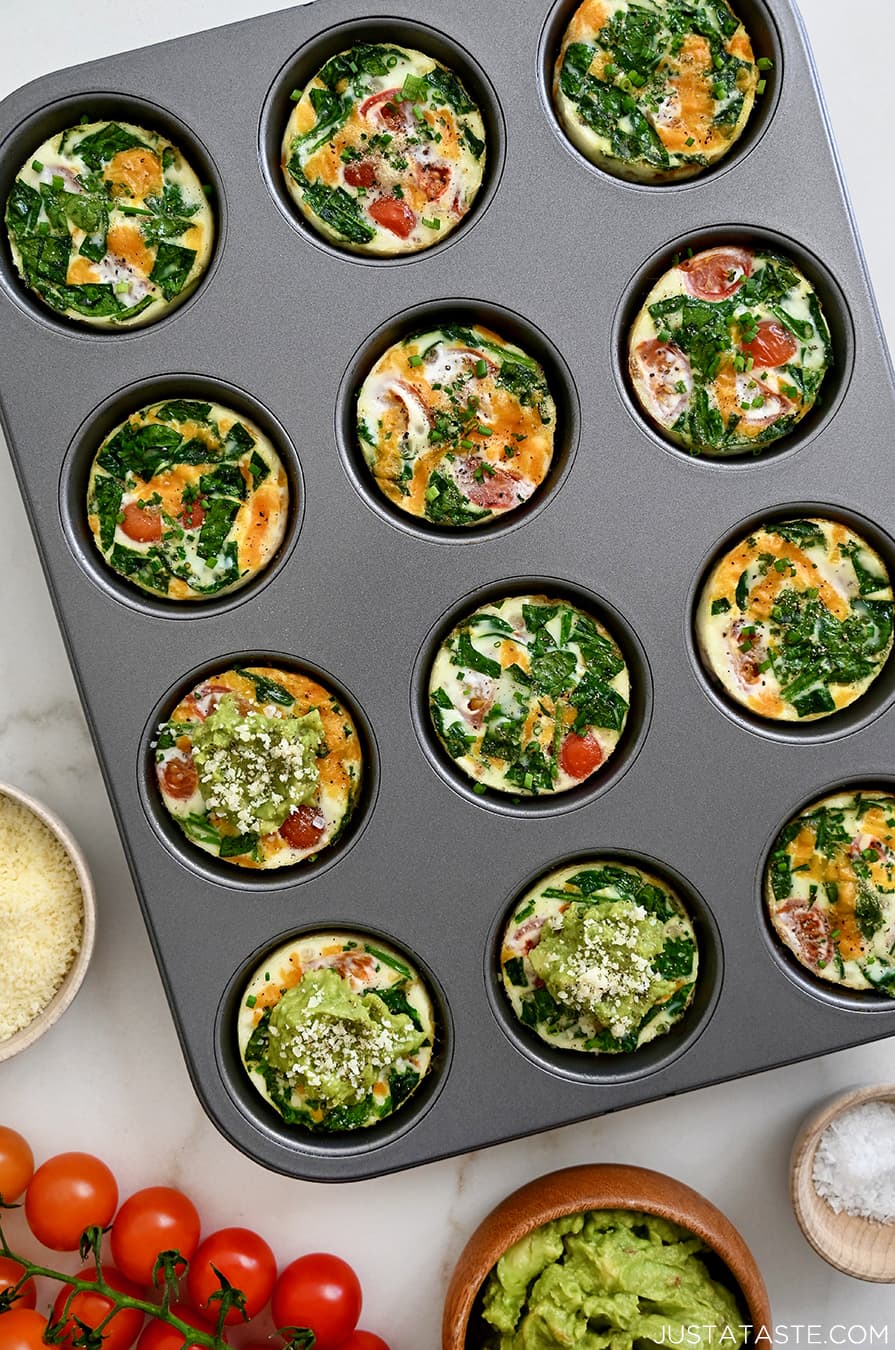 A top-down view of a muffin pan with egg white muffins, tomatoes and avocado
