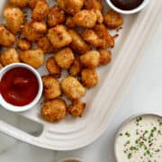 Chicken nuggets on a serving plate with small ramekins containing barbecue sauce and ketchup.