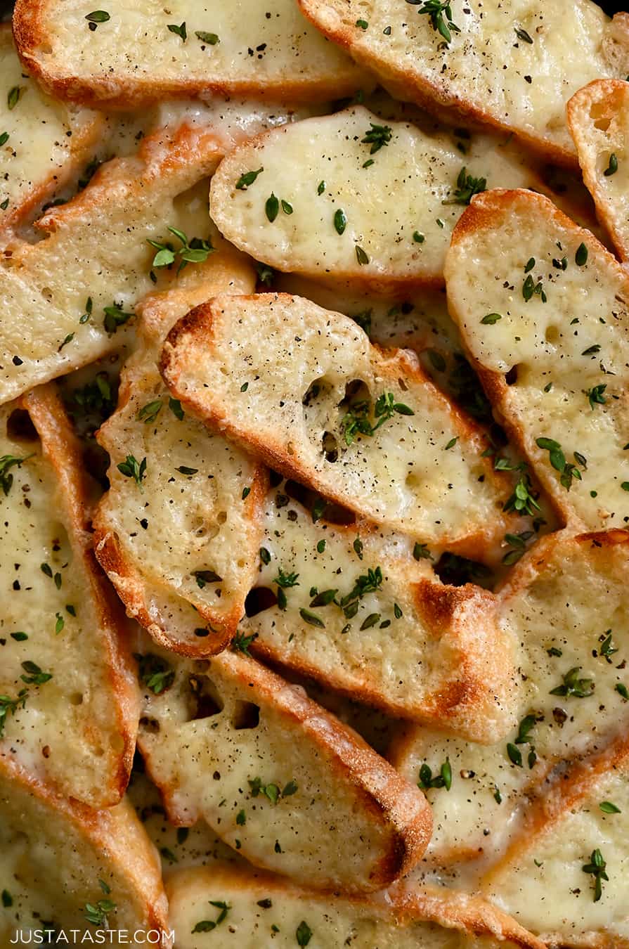 A close-up of toasts topped with melted gruyere cheese and fresh thyme