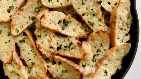 A blue skillet containing cheesy toasts surrounded by small bowls