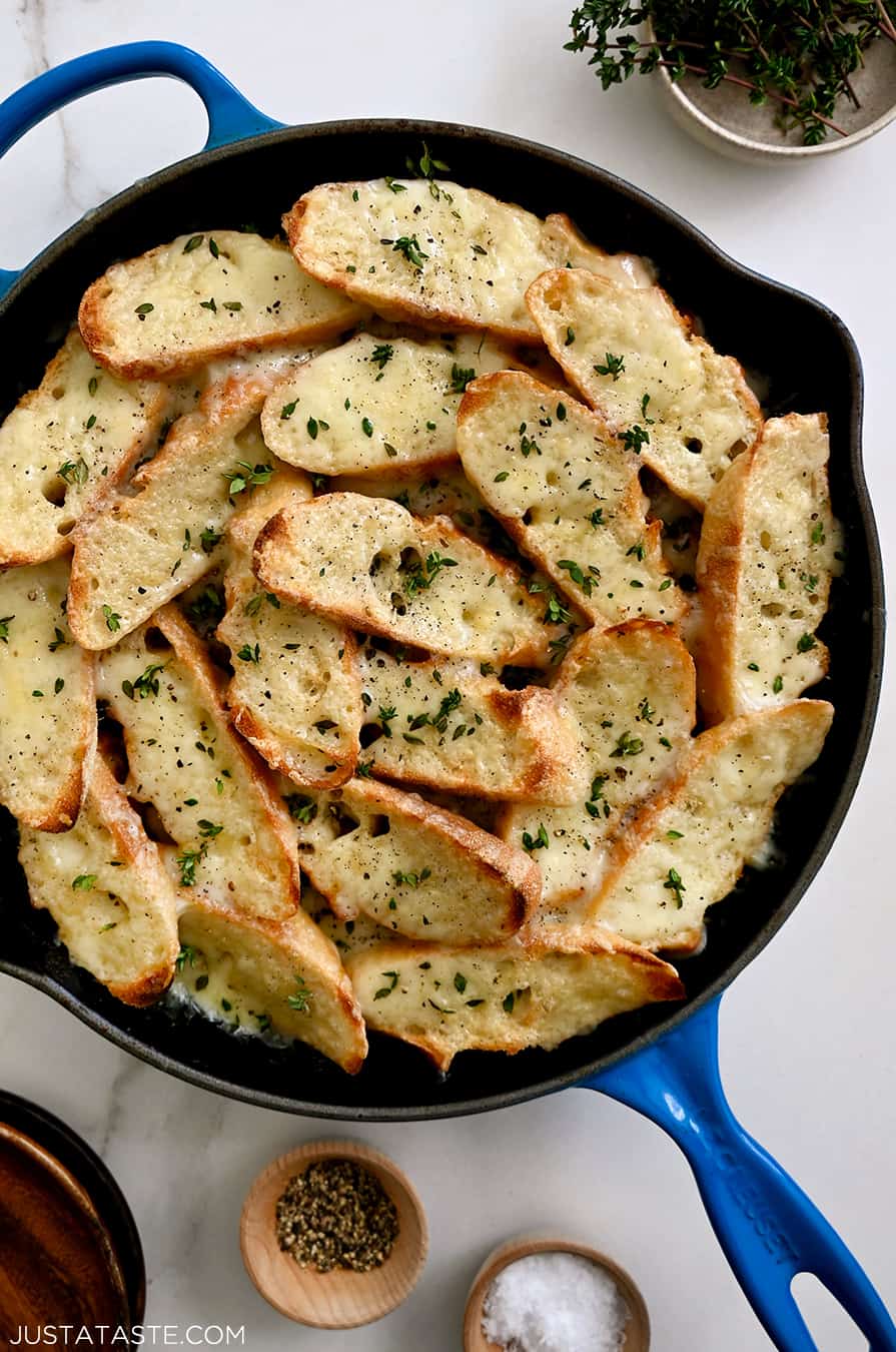 A blue skillet containing cheesy toasts surrounded by small bowls