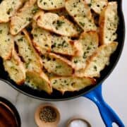 A top-down view of a blue skillet containing cheesy toasts surrounded by small bowls.