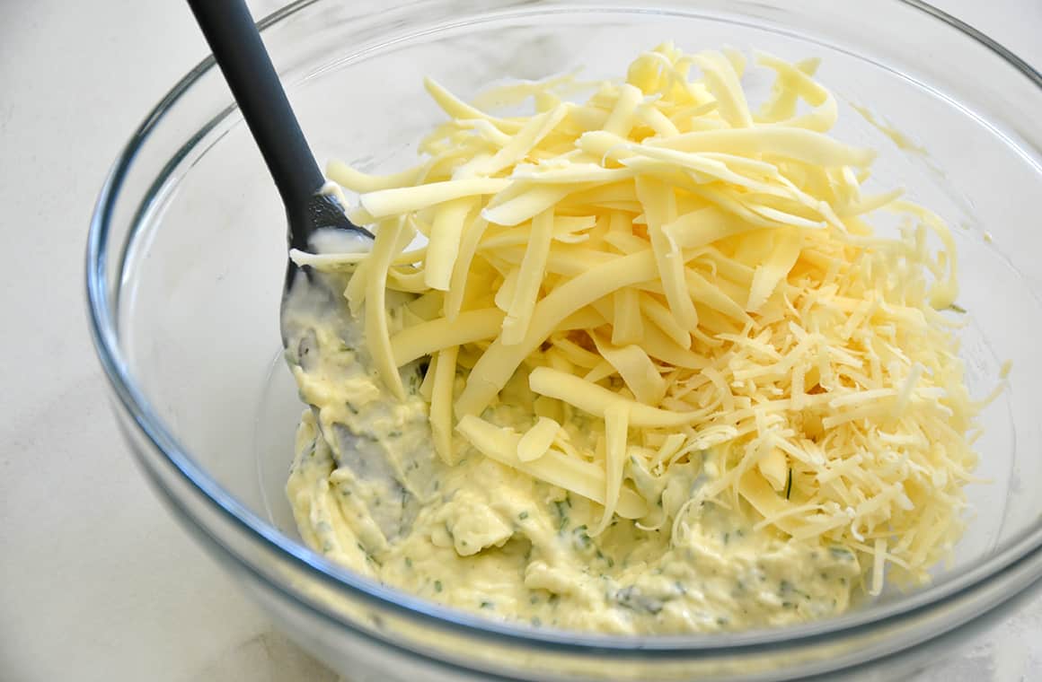 A clear bowl containing garlic butter and mayonnaise mixture topped with shredded mozzarella cheese