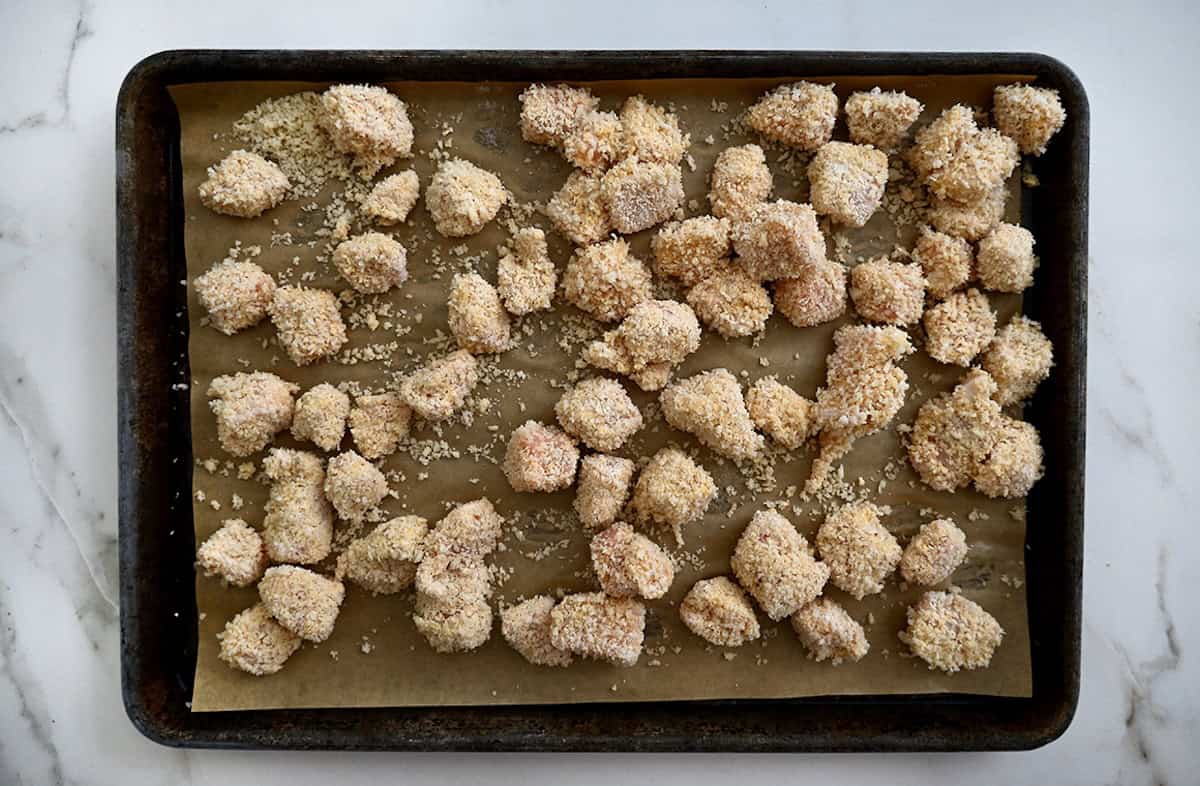 Breaded, uncooked chicken nuggets on a parchment paper-lined baking sheet.