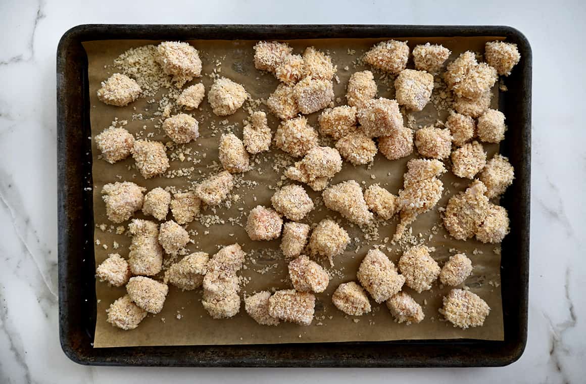 A baking sheet lined with parchment paper and topped with uncooked chicken nuggets