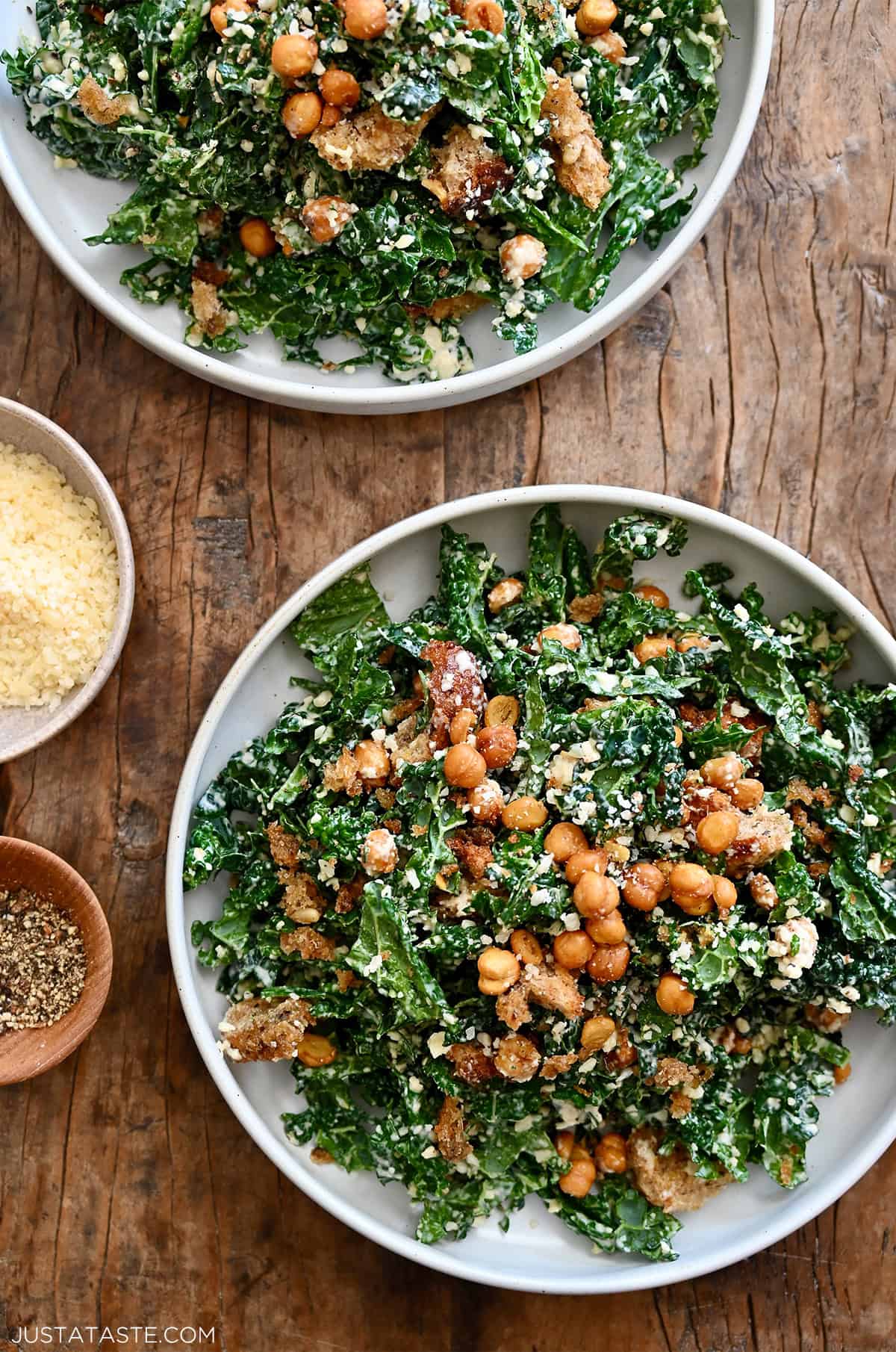 Two plates containing kale salad tossed with homemade Caesar dressing, topped with croutons and crispy chickpeas.