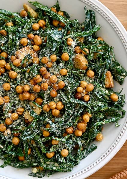A top-down view of kale salad in a white bowl with lemons and a small bowl of Parmesan cheese on the side
