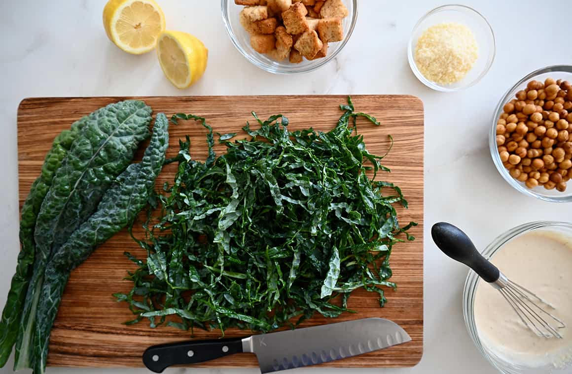 A wood cutting board topped with shredded kale and small bowls surrounding it