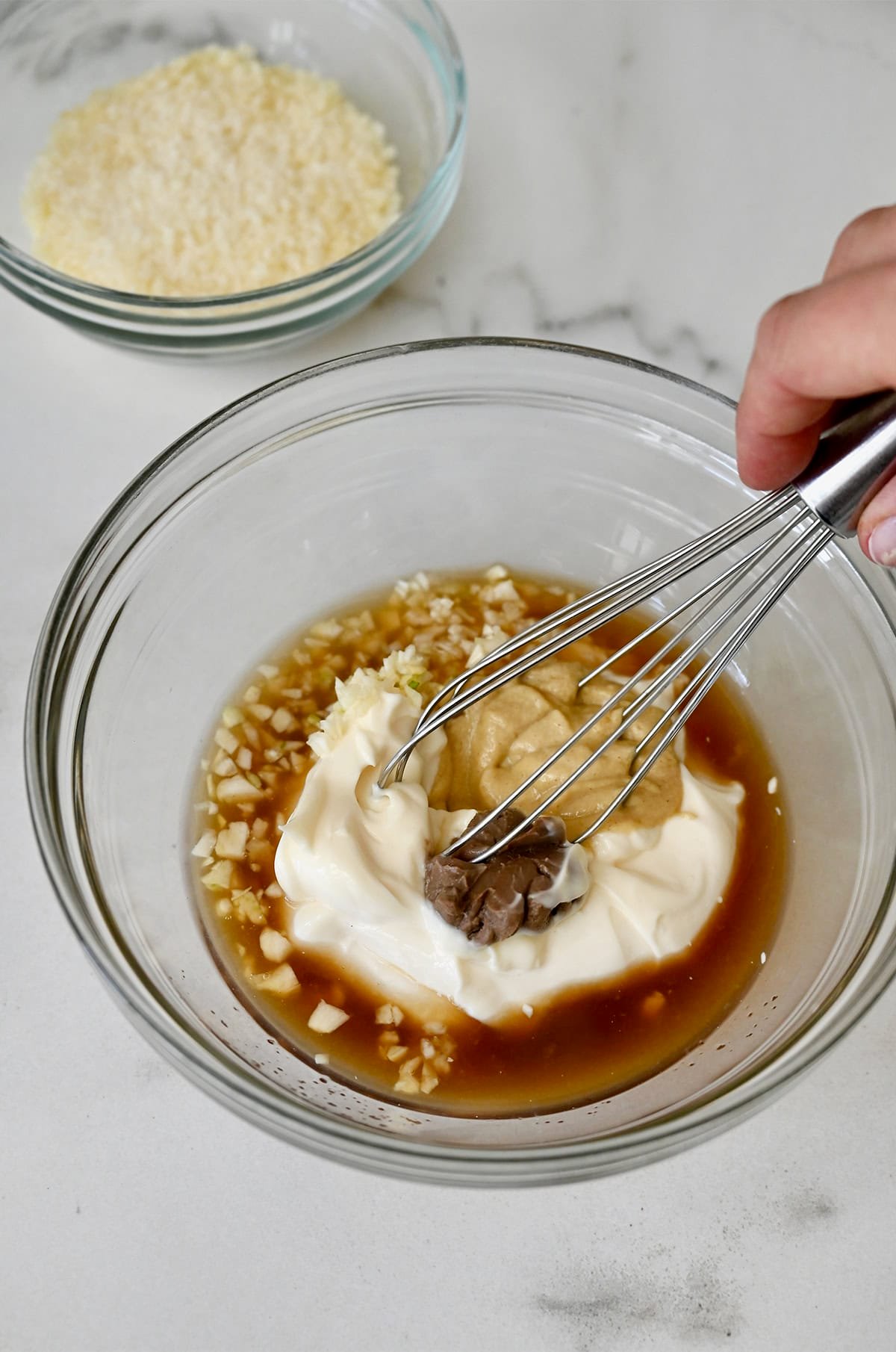 Whisking together Dijon mustard, lemon juice, Worcestershire sauce, mayonnaise, garlic, and anchovy paste in a bowl to make homemade Caesar dressing.