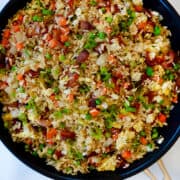 A top-down view of a non-stick skillet containing Bacon and Egg Fried Rice with onions, peas and carrots.