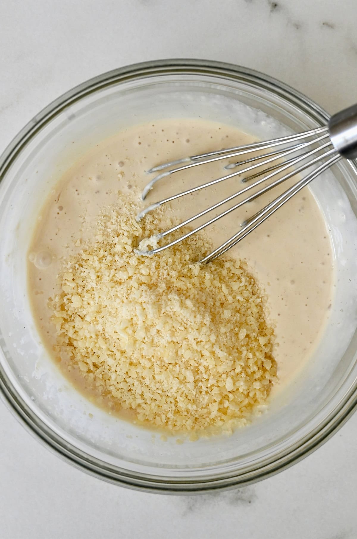 Whisking grated Parmesan cheese into a homemade Caesar salad dressing in a bowl.