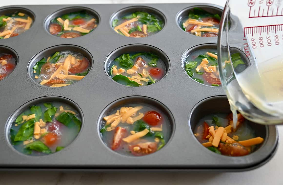 A liquid measuring cup pouring egg whites into a muffin tin