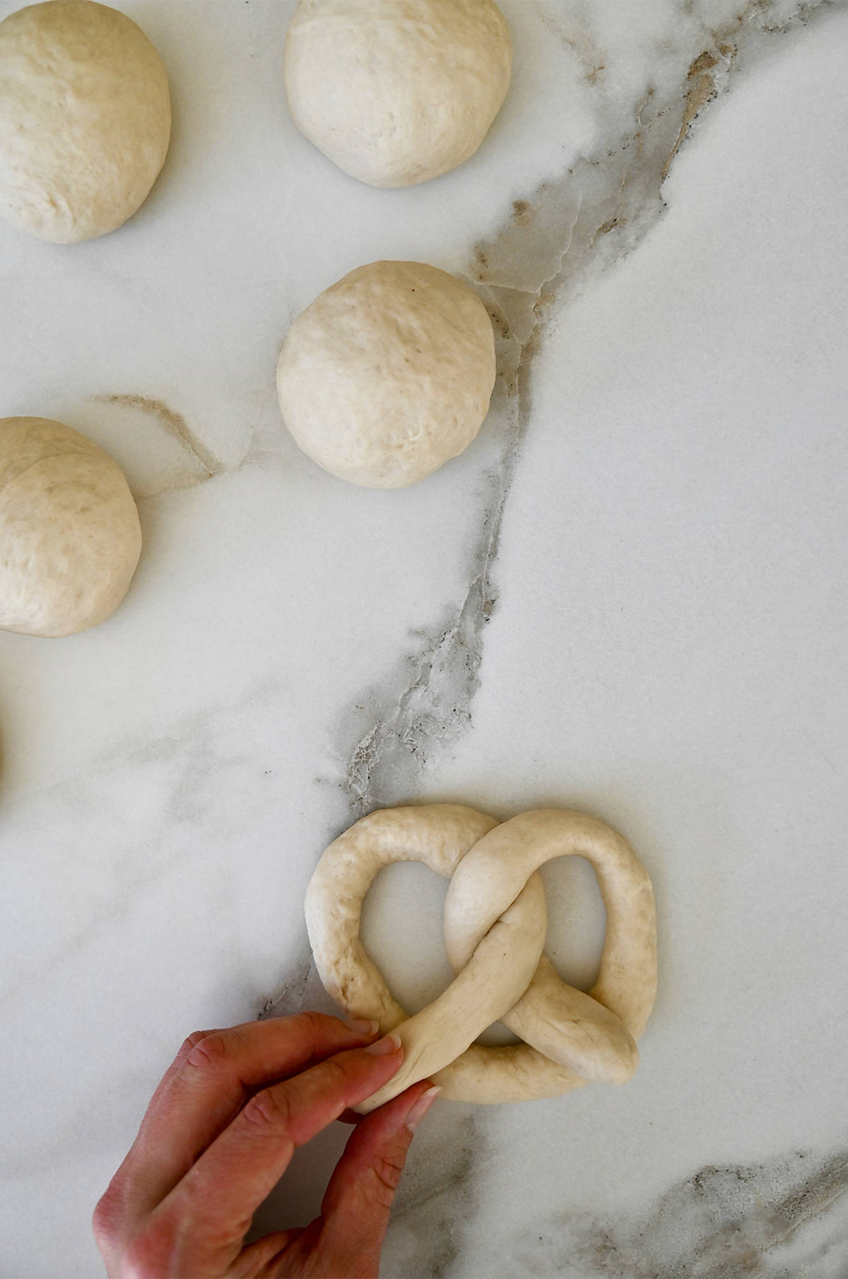 A hand twists dough into a classic pretzel shape.