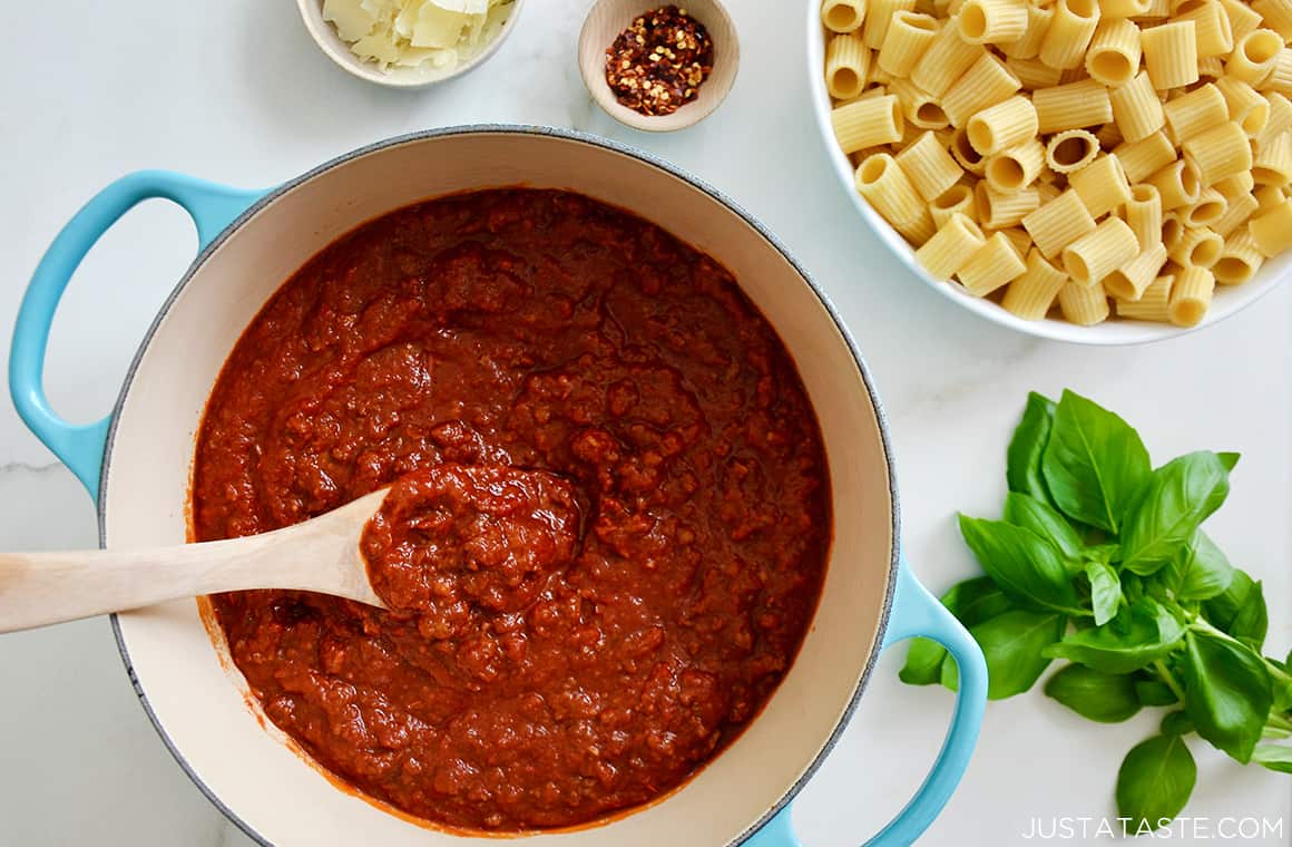 A top-down view of the best homemade Bolognese Sauce in a large stock pot next to a bowl with rigatoni 