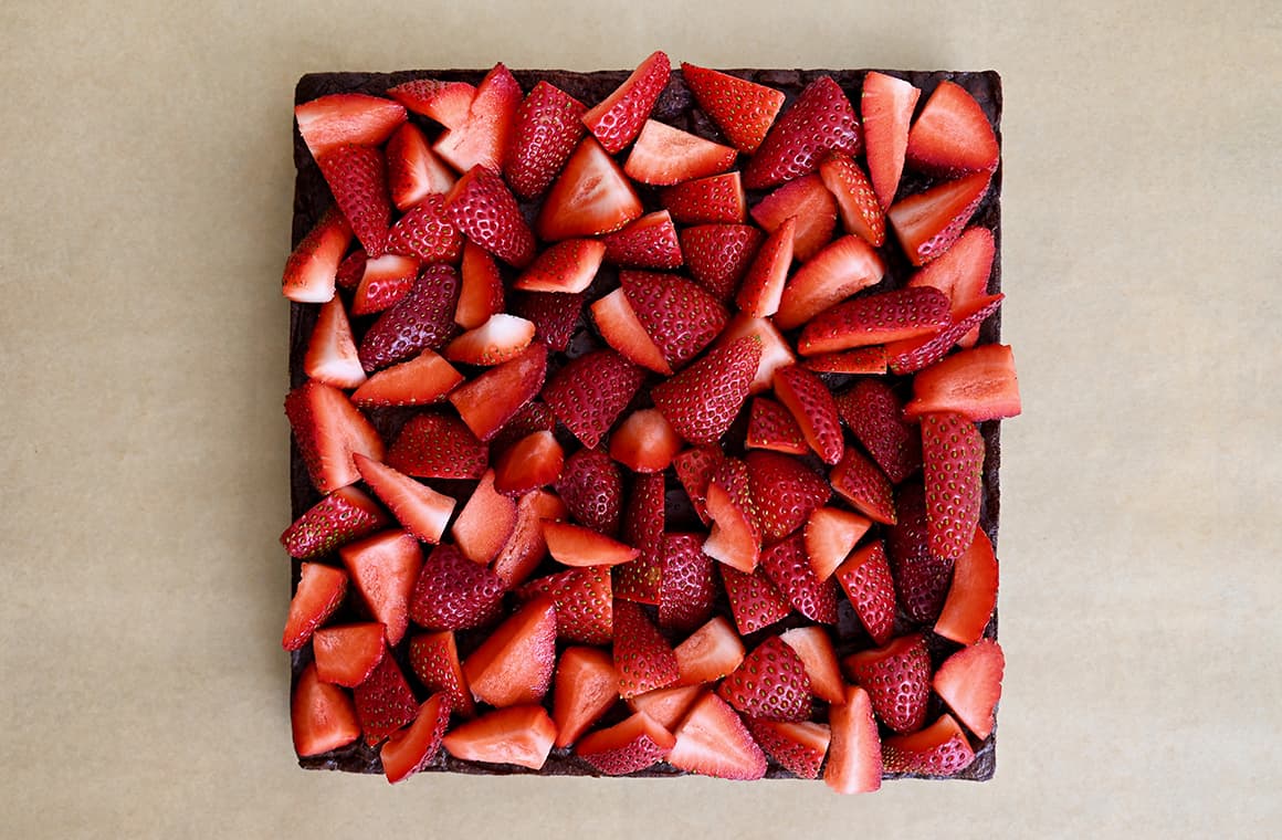A top-down view of sliced strawberries atop brownies