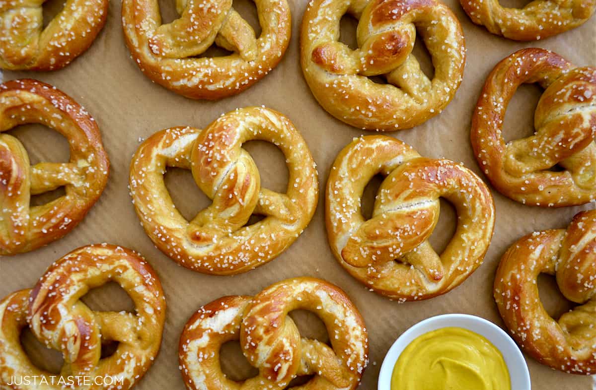 Golden brown iconically-shaped soft pretzels topped with salt next to a small bowl filled with yellow mustard.