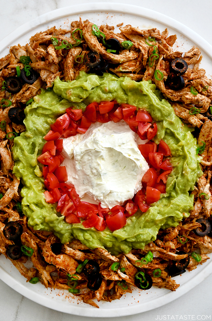 A close-up view of chicken taco dip featuring cream cheese, tomatoes, guacamole and black olives