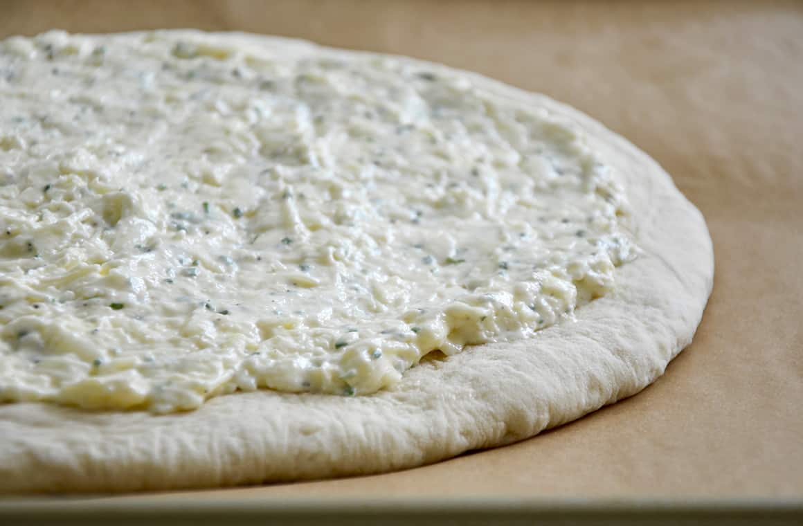 Pizza dough topped with garlic cheese mixture atop parchment paper