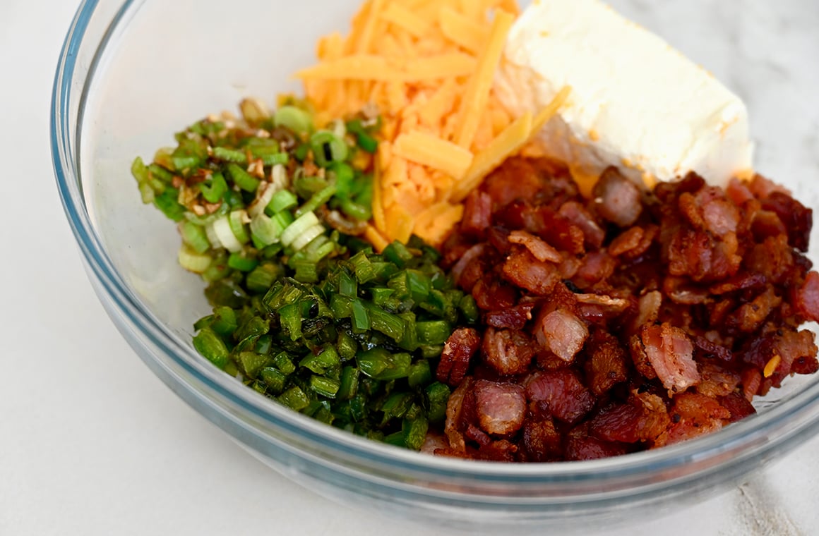 A glass bowl with cream cheese, cheddar cheese, jalapeños, bacon and scallions 