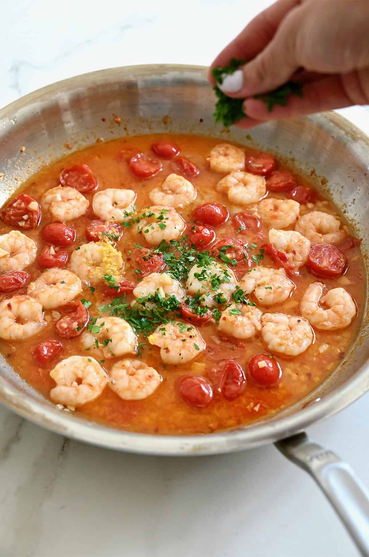 Adding diced fresh parsley to shrimp scampi in a skillet.