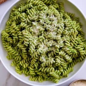 A large serving bowl containing Broccoli Pesto Pasta garnished with parmesan cheese