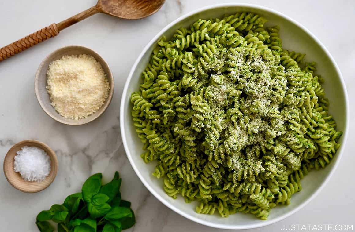 A top-down view of a large white serving bowl with rotini pasta tossed with broccoli pesto