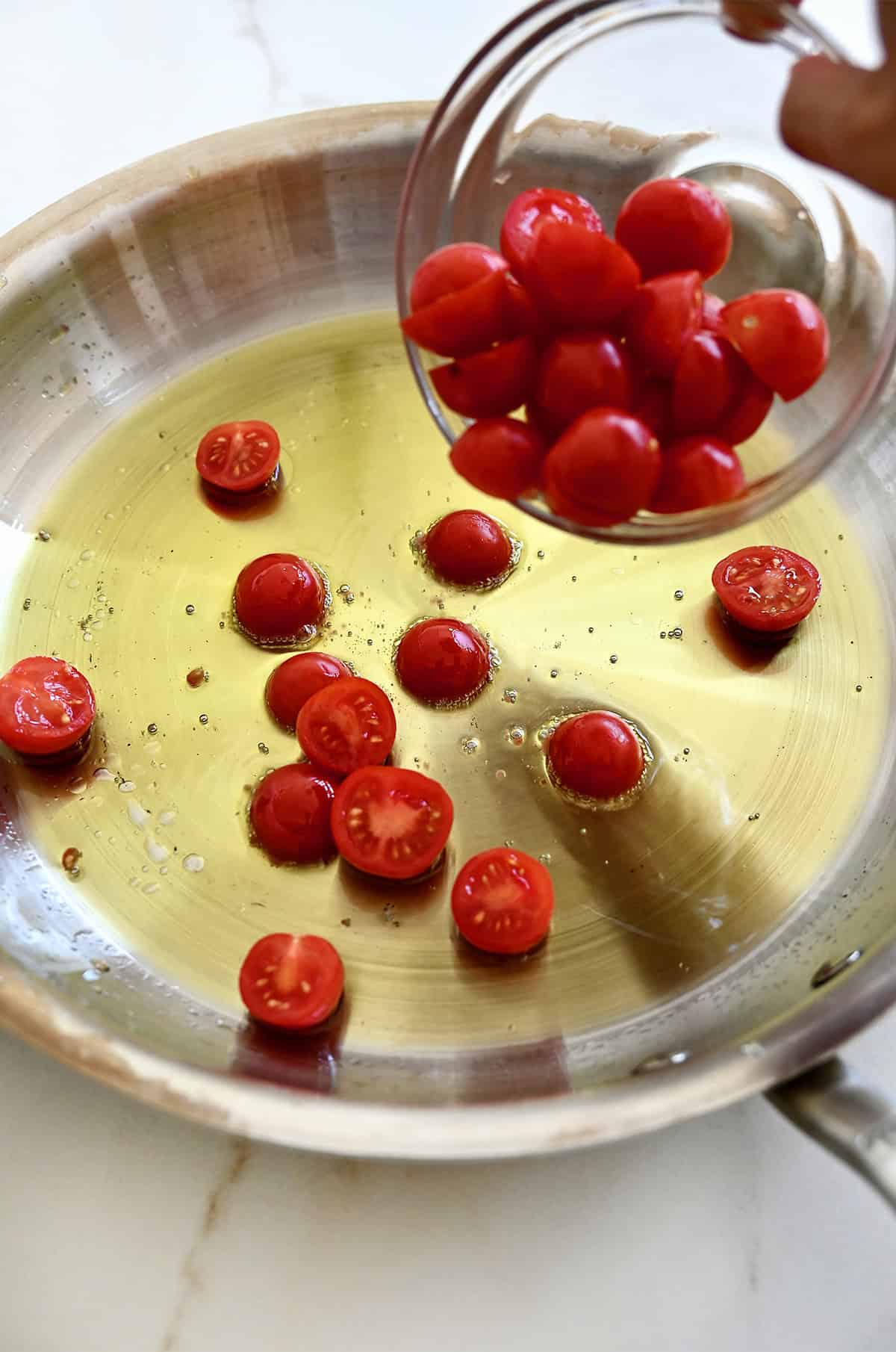 Halved cherry tomatoes are being added to a skillet with oil.