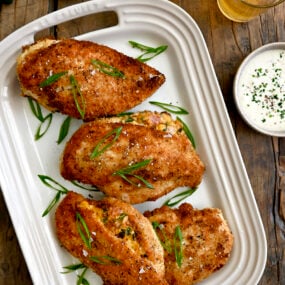 A white platter containing Stuffed Jalapeno Popper Chicken breasts with scallions