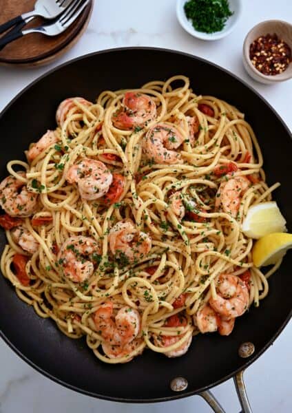 A large skillet containing Quick Shrimp Scampi with cherry tomatoes, chili flakes and fresh herbs.