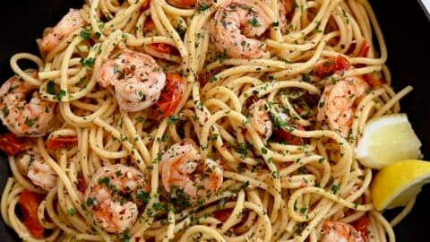 A large skillet containing Quick Shrimp Scampi with cherry tomatoes, chili flakes and fresh herbs.