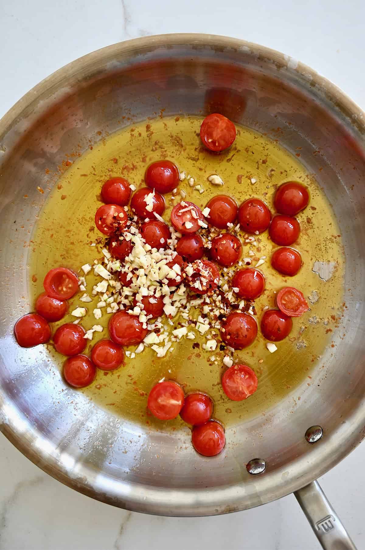 Sautéed garlic and tomatoes in a stainless steel skillet with olive oil.