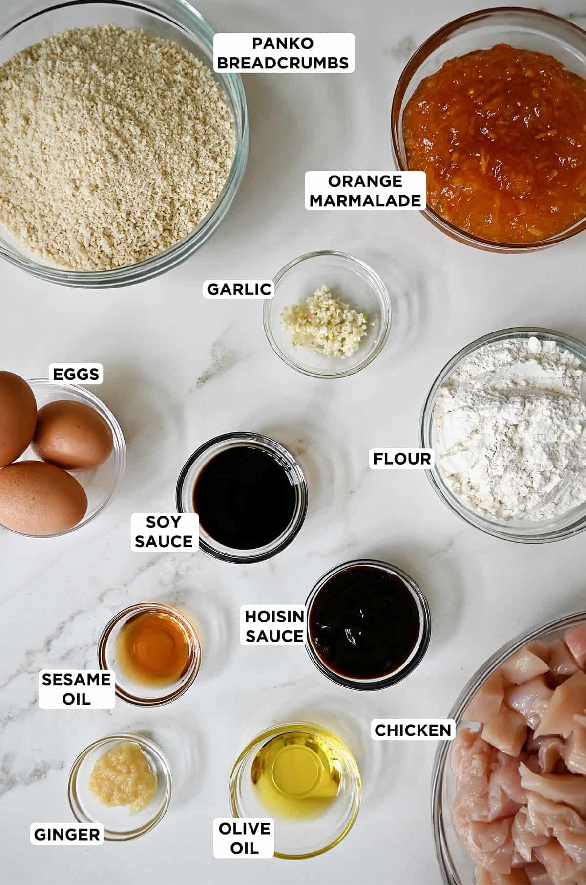 Orange chicken ingredients, including orange marmalade, hoisin sauce, soy sauce, sesame oil, chicken breasts, eggs, flour, Panko breadcrumbs, minced garlic and ginger.