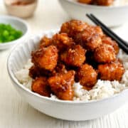 Baked Orange Chicken atop white rice in a bowl with chopsticks.